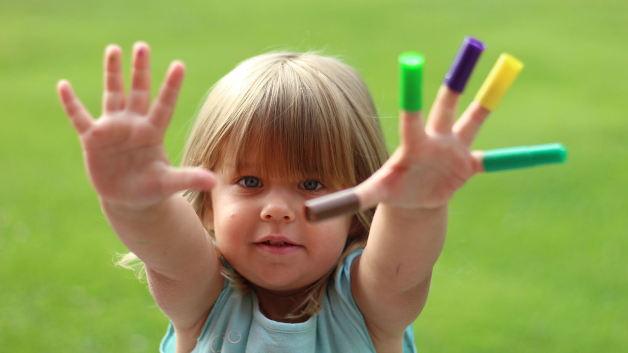 Barn som visar tio fingrar. På fem av dem sitter korkar från tuschpennor.