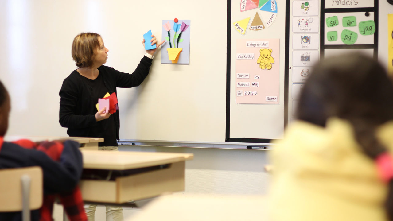 Lärare som visar på vita tavlan. Elever i förgrunden.