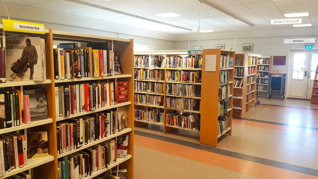 Inne på ett bibliotek. Bokhyllor i trä med böcker.