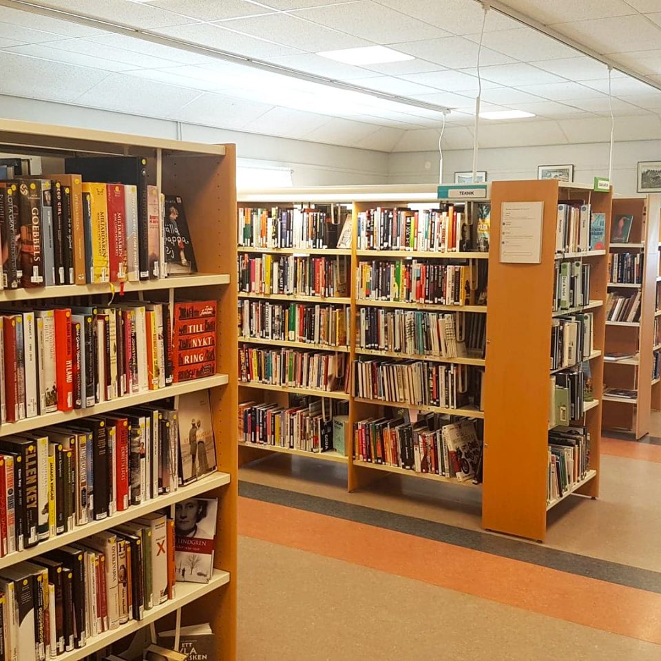 Inne på ett bibliotek. Bokhyllor i trä med böcker.