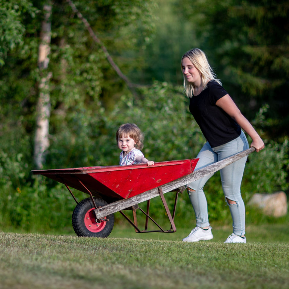Större tjej som skjutsar yngre i en röd skottkärra.