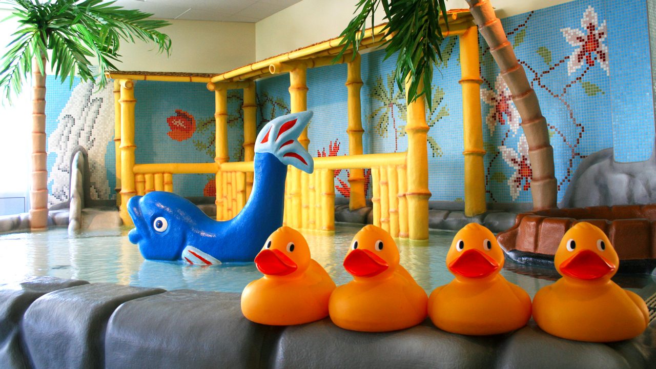 Gula badankor i förgrunden. Barnbassäng med palmer i bakgrunden.