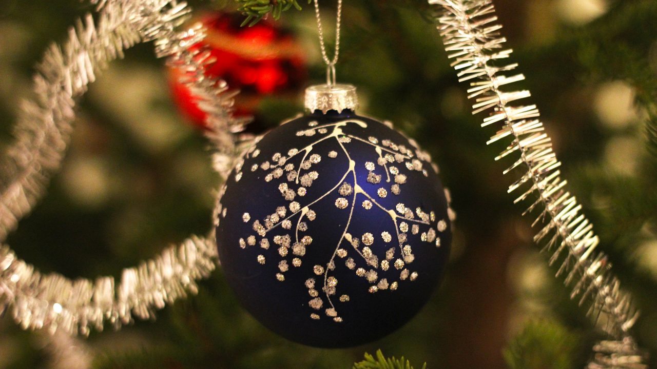 Närbild på en mörkblå julgranskula med silverpluppar. Gran och glitter i bakgrunden.