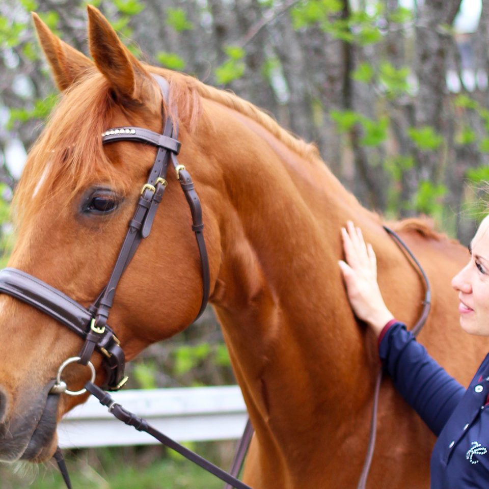 En kvinna står bredvid sin häst och tittar på den.