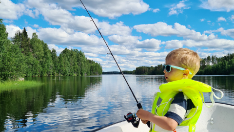 Barn med gul flytväst som sitter i båt och fiskar.