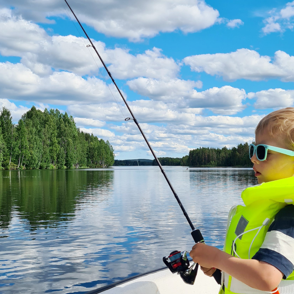 Barn med gul flytväst som sitter i båt och fiskar.