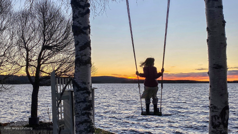 Barn som står på gunga. Vatten i bakgrunden.