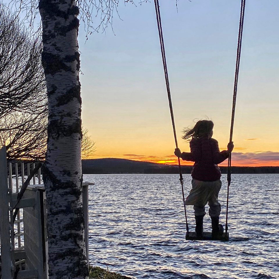 Barn som står på gunga. Vatten i bakgrunden.