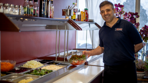 Man som står vid en buffé. Han håller i en skål och ser glad ut.