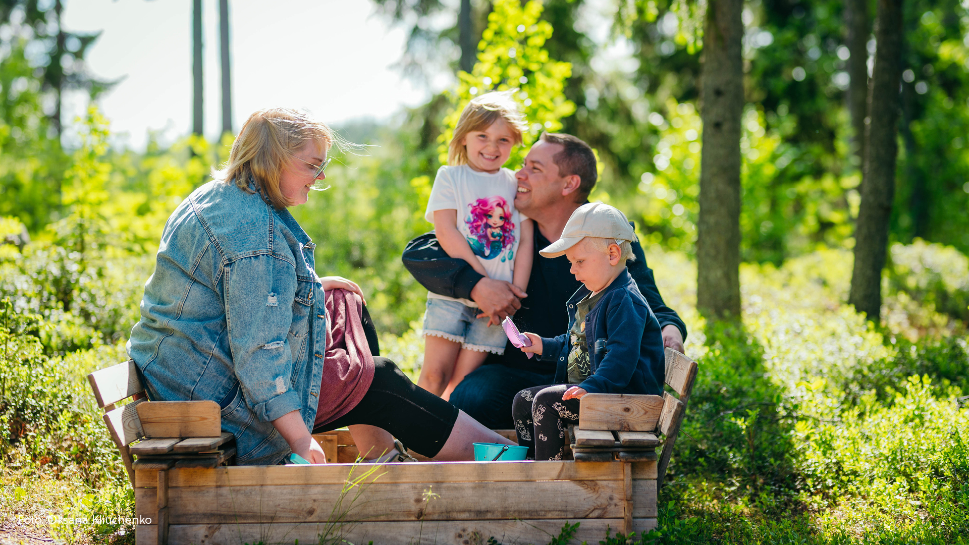 Två barn och två vuxna i en sandlåda.