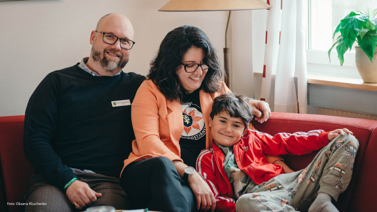Mamma, pappa och barn i en röd soffa.