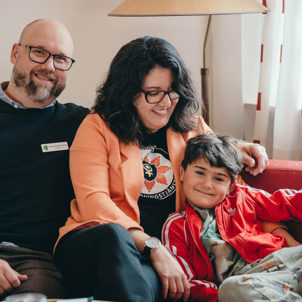 Mamma, pappa och barn i en röd soffa.